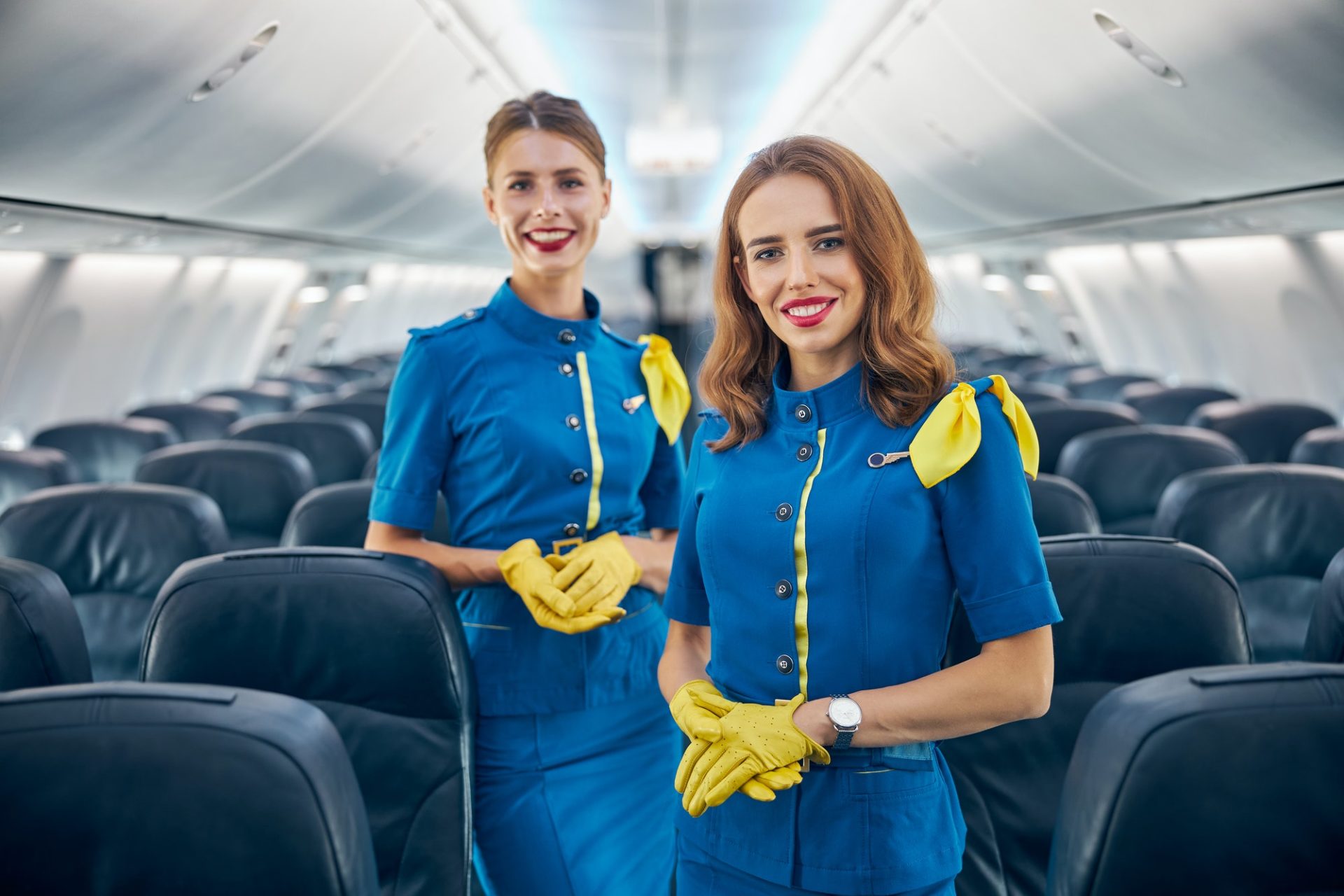 two-women-flight-attendants-smiling-at-the-photo-camera-in-salon-of-passenger-aircraft-e1630651564416.jpg